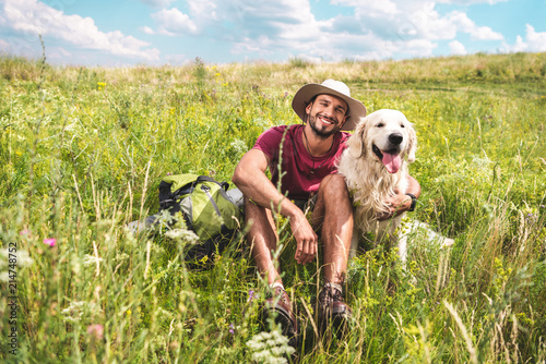 male traveler sitting with dog on green summer meadow