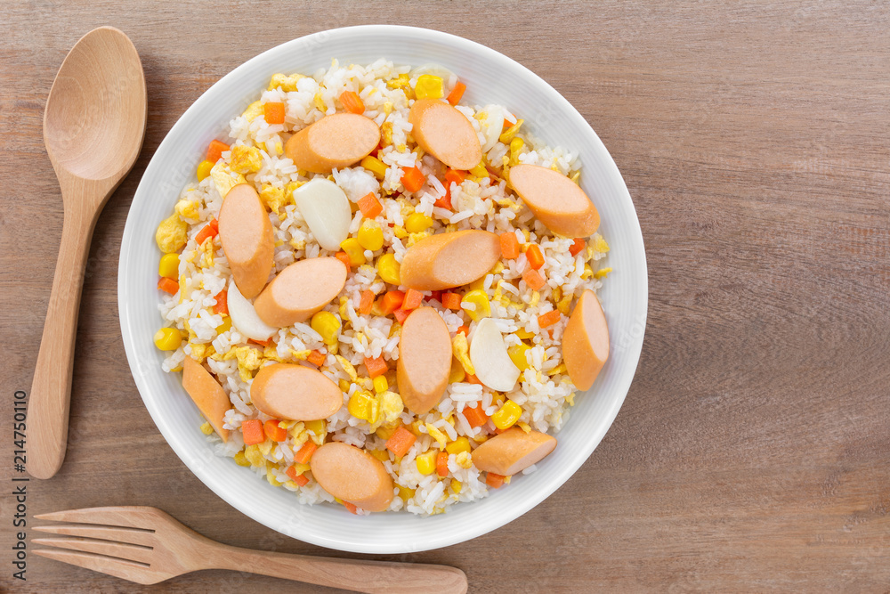 top view of fried rice with sausage and vegetable in a ceramic dish on wooden table. homemade style food concept.