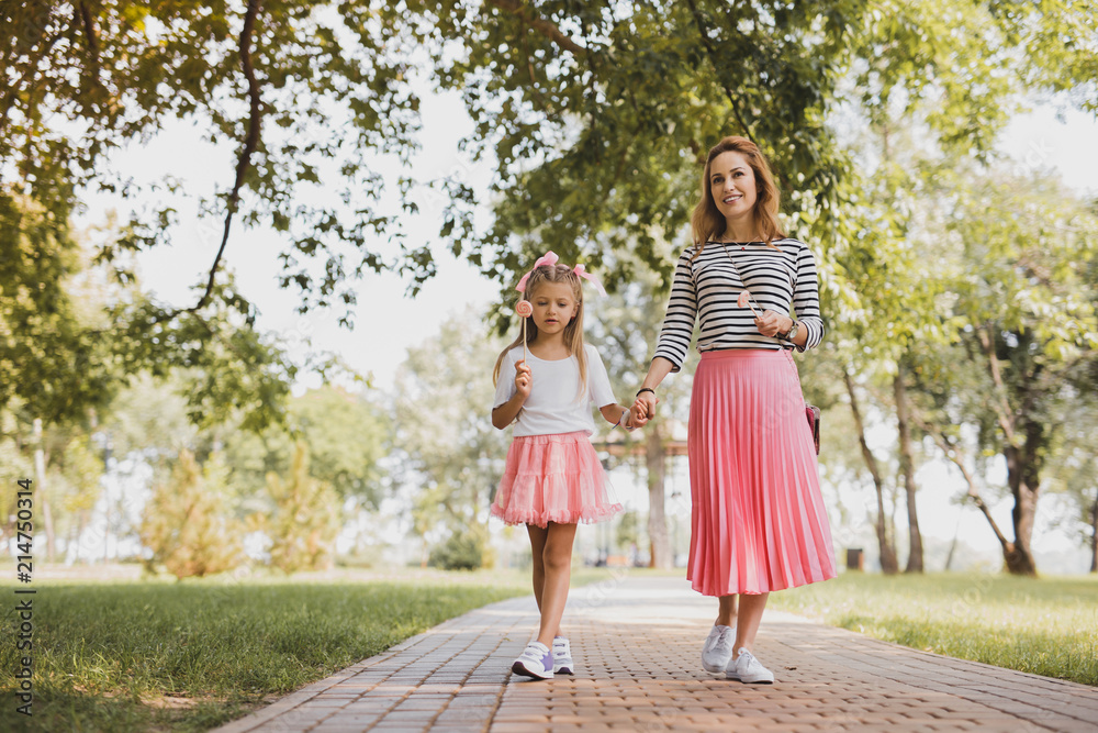 Walking with mother. Cute beautiful girl wearing short pink skirt with lollipop in her hand walking with mother Walking with mother. Cute beautiful girl wearing short pink skirt with lollipop in her hand walking with mother