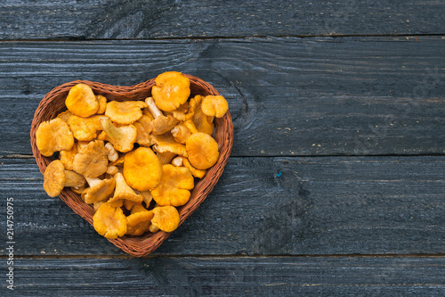 Orange chanterelle mushrooms lie in a wooden basket in the shape of a heart on a black background