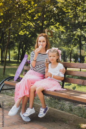 Fashionable sneakers. Stylish mother and daughter wearing fashionable sneakers while sitting on bench in the park