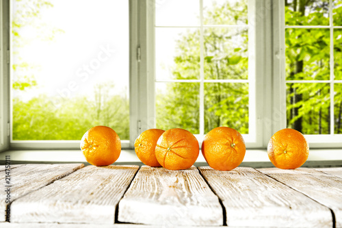 Fresh orange fruits on white wooden table and free space for your bottle or glass. Window background with summer garden landscape. 