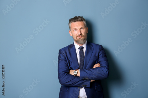 Handsome mature man in elegant suit on color background
