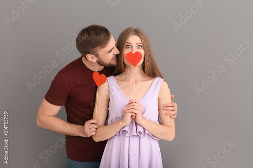 Happy young couple with red hearts on grey background