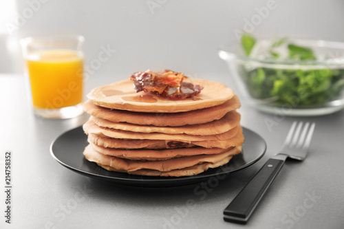Plate with tasty pancakes and bacon on light table