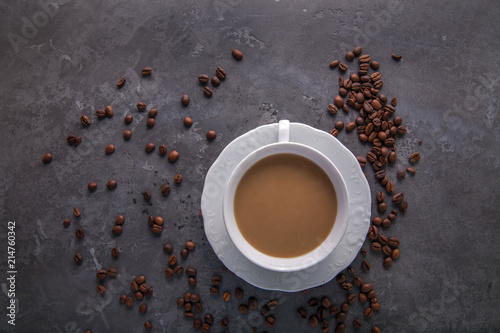  White cup of coffee with milk or tea with milk on dark grey beton background decorated with coffee beans. Copy space