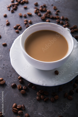  White cup of coffee with milk or tea with milk on dark grey beton background decorated with coffee beans. Copy space