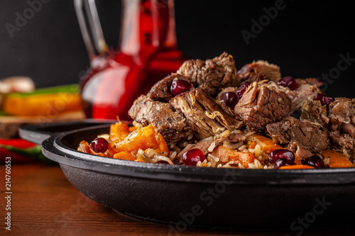 Uzbek traditional cuisine. Pilaf or plov with lamb, and red garnet, in an iron cast-iron frying pan kazan. Background image. Copy space, selective focus