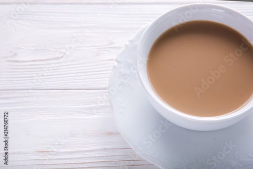  White cup of coffee with milk or tea with milk on white wooden background decorated with coffee beans. Copy space