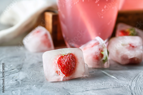 Ice cubes with frozen strawberries on table