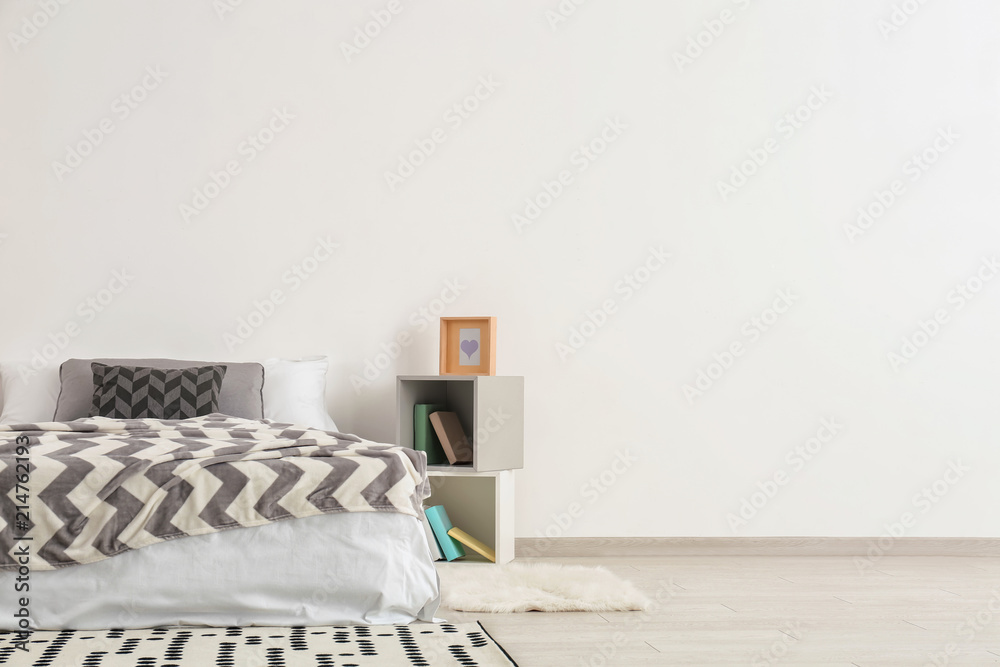 Fototapeta premium Big comfortable bed with shelf unit near light wall