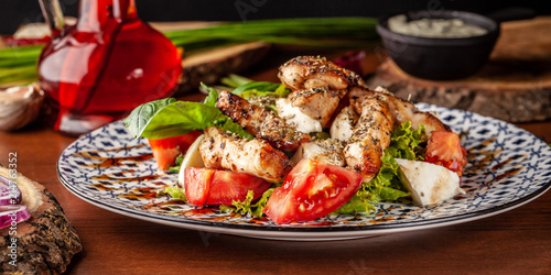 Uzbek traditional cuisine. Salad Zarafshon from roasted chicken fillet, mozzarella cheese, tomatoes, lettuce leaves, olive oil, mustard sauce. Background image. Copy space, selective focus photo