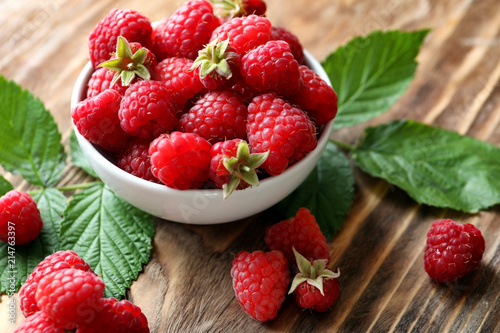 Bowl with ripe aromatic raspberries on wooden background