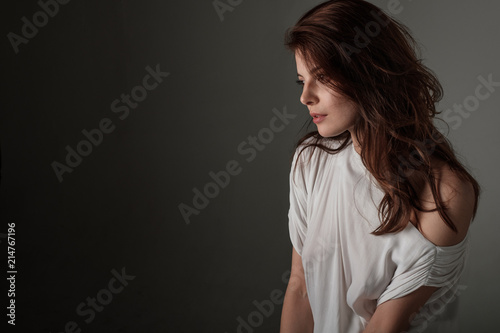 A beautiful brunette girl with her hair down in a white tunic stands in a half-turn.The photo can be used as a wallpapper.