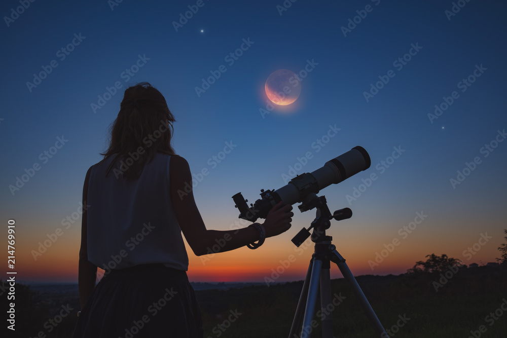 Obraz premium Girl looking at lunar eclipse through a telescope. My astronomy work.