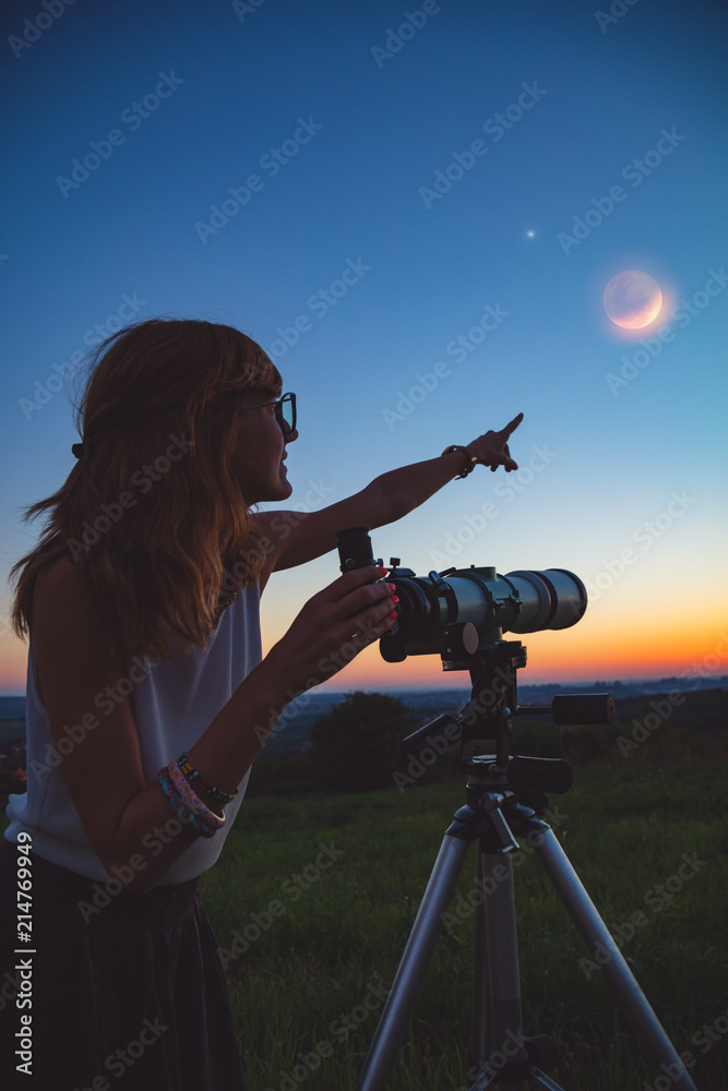 Naklejka premium Girl looking at lunar eclipse through a telescope. My astronomy work.