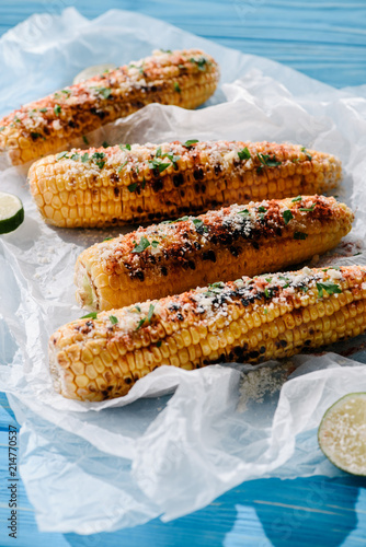 close up view of delicious grilled corn with lime slices on baking paper on wooden table