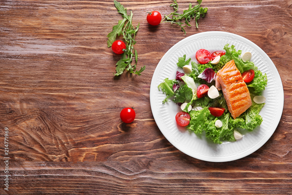 Plate with tasty grilled fish and fresh salad on wooden table Plate with tasty grilled fish and fresh salad on wooden table