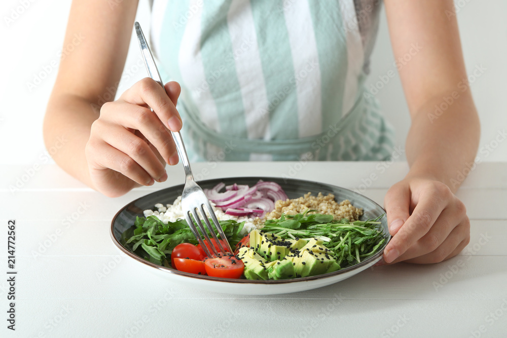 Young woman eating delicious healthy fresh salad at wooden table