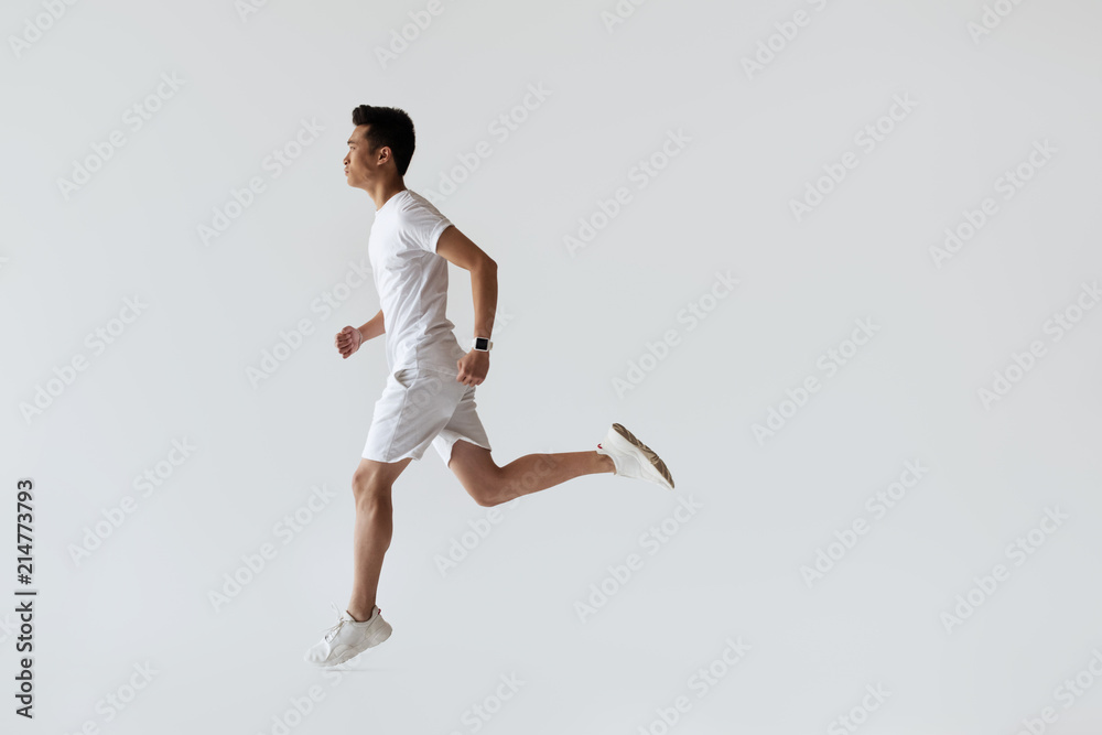 side view of young asian jogger running on grey background