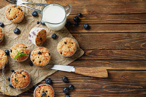 Tasty blueberry muffins and jug of milk on wooden table