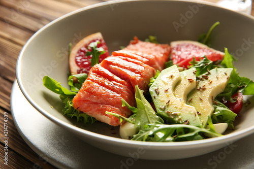 Bowl with fresh salad and fish on wooden table, closeup