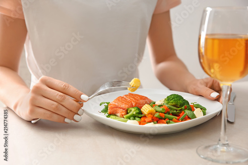Woman eating fresh salad and fish at light table
