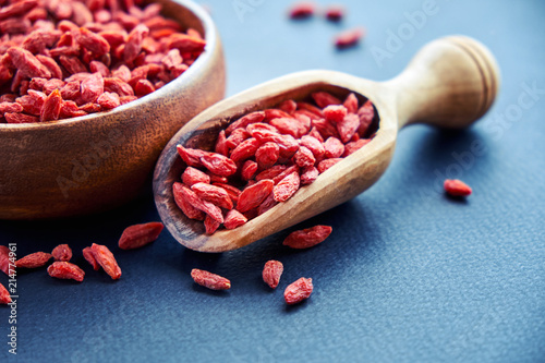 Goji in bowl on wood table. Top view of fresh goji in scoop and bowl. Goji in heart shape on table photo