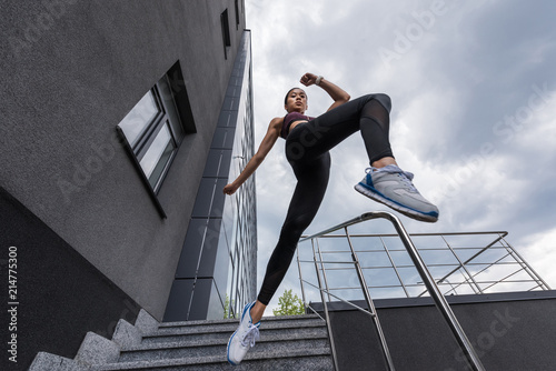 Принти на полотні low angle view of asian sportswoman jumping from stairs at urban street
