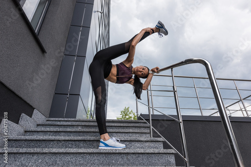 young asian sportswoman stretching on stairs at urban street