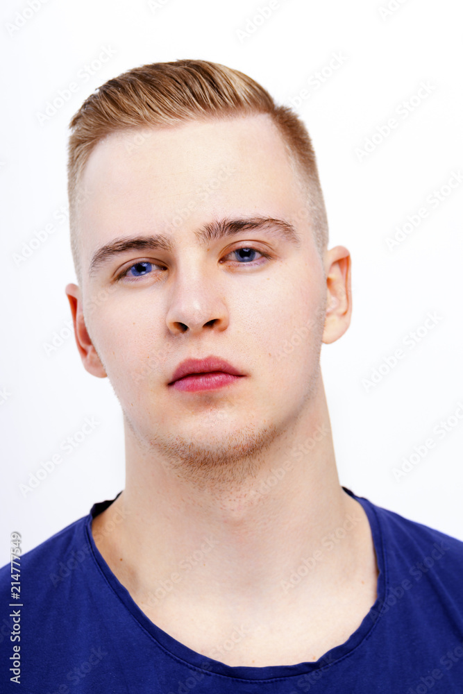 Fototapeta premium Young blond man in blue shirt poses in studio, close up portrait
