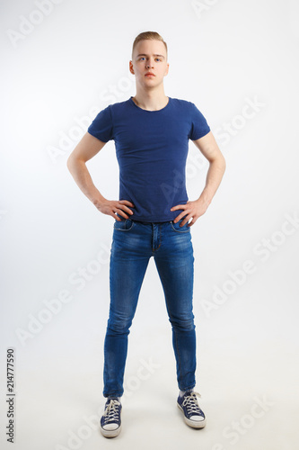 Young handsome man in blue shirt and jeans poses in white studio, full body