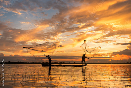 Two fisherman cast a net at lake in the moring time , silhouette light