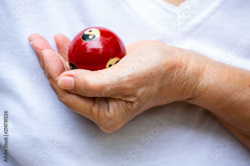 Senior woman's hand holding a black and white Yin Yang religious symbol on red ball in Taoism isolated on white background