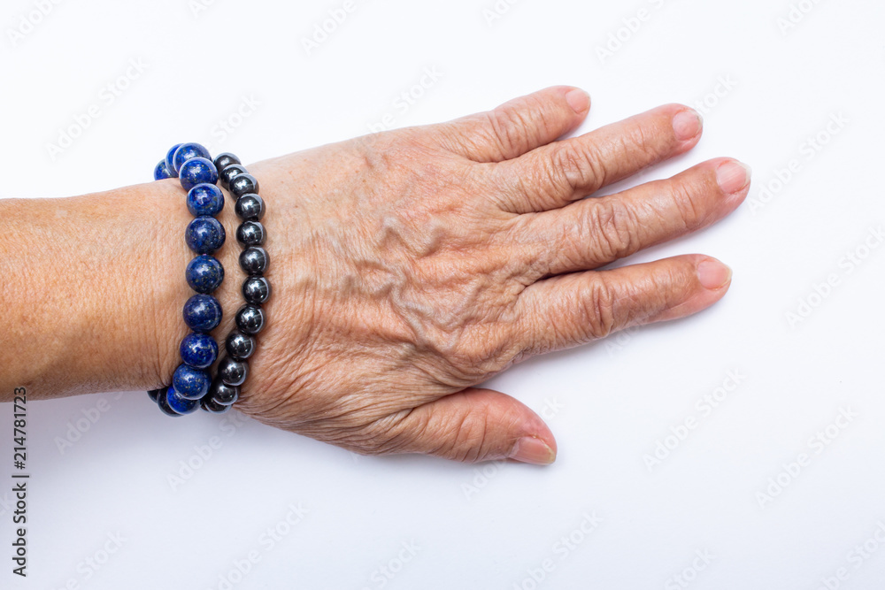 Fototapeta premium Senior woman's hand wearing supplement good fortune colorful bracelets isolated on white background