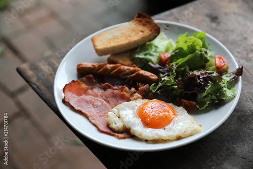 English breakfast  fried egg, ham,sausage, bacon,salad and toast on wood background in mystic light