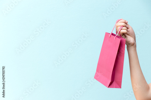 Hand of business woman hold pink shopping bag on blue concrete background