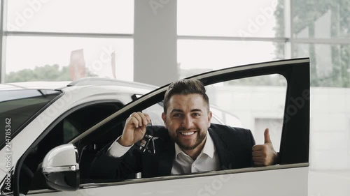 Young business man is smiling, showing thimb up and the keys of his just purchased car. photo