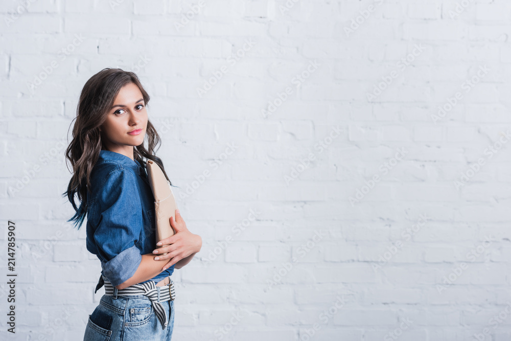 attractive young woman holding paper package in front of brick wall attractive young woman holding paper package in front of brick wall
