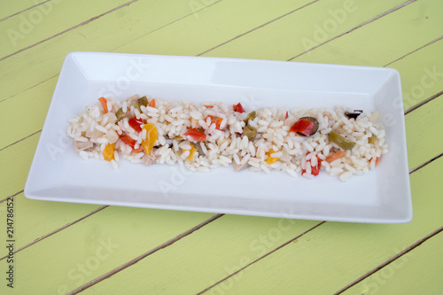 Rice salad in a white tray on a green wooden table seen close up