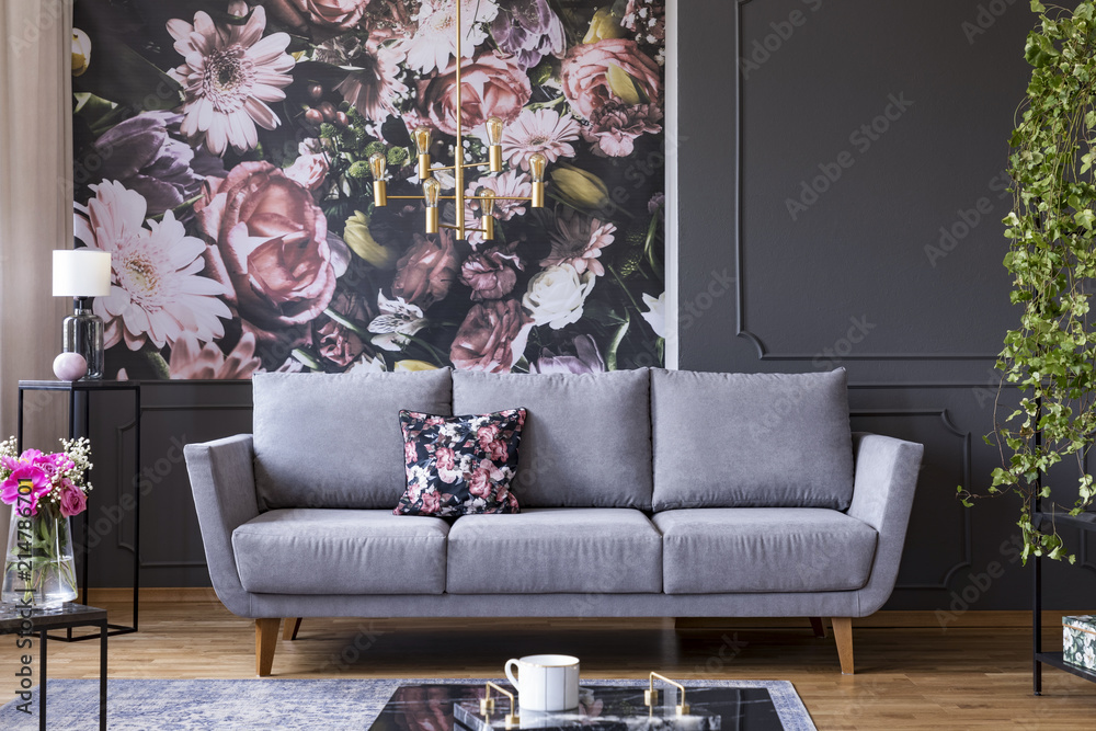 Fototapeta Grey lounge with patterned cushion in real photo of dark living room interior with floral wallpaper, molding on wall and gold lamp