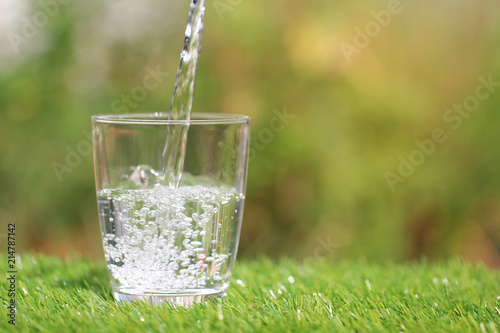 Closeup of pouring pure water from bottle into glass on table natural green background