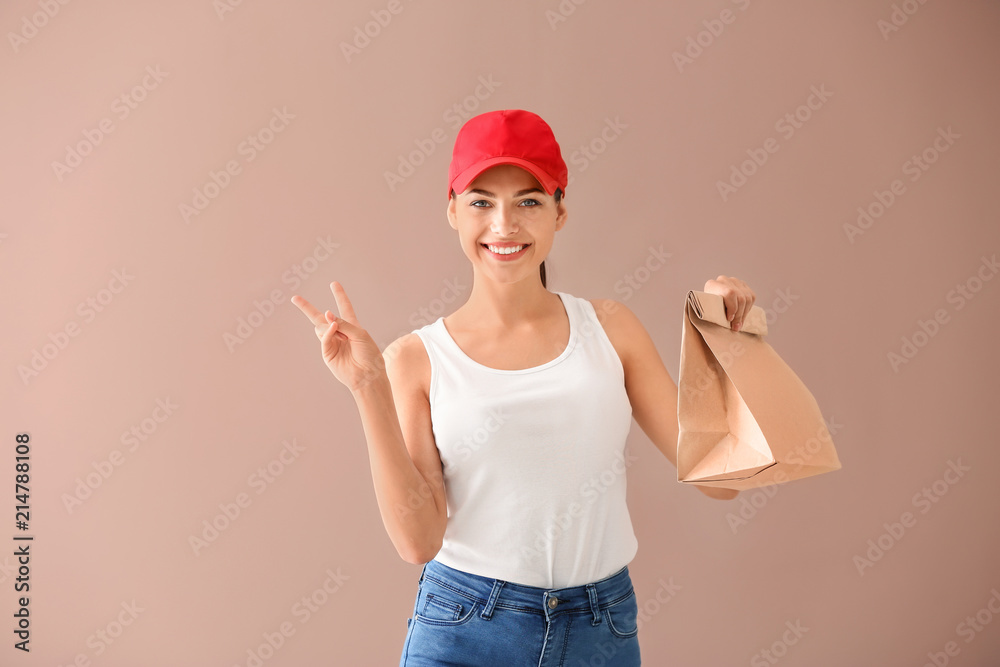 Young woman with paper bag showing victory sign on color background. Food delivery service