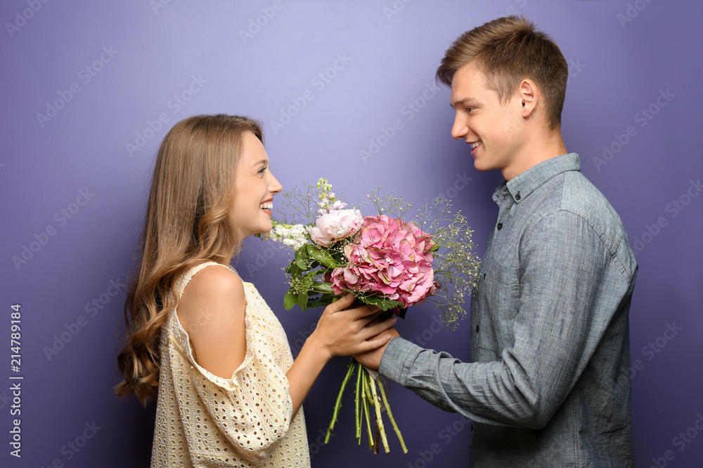 Young man giving beautiful flowers to his beloved girlfriend on color background