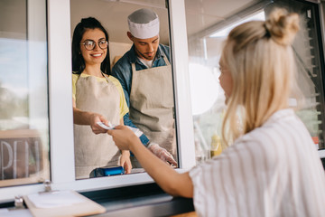 young woman paying to smiling worker in food truck