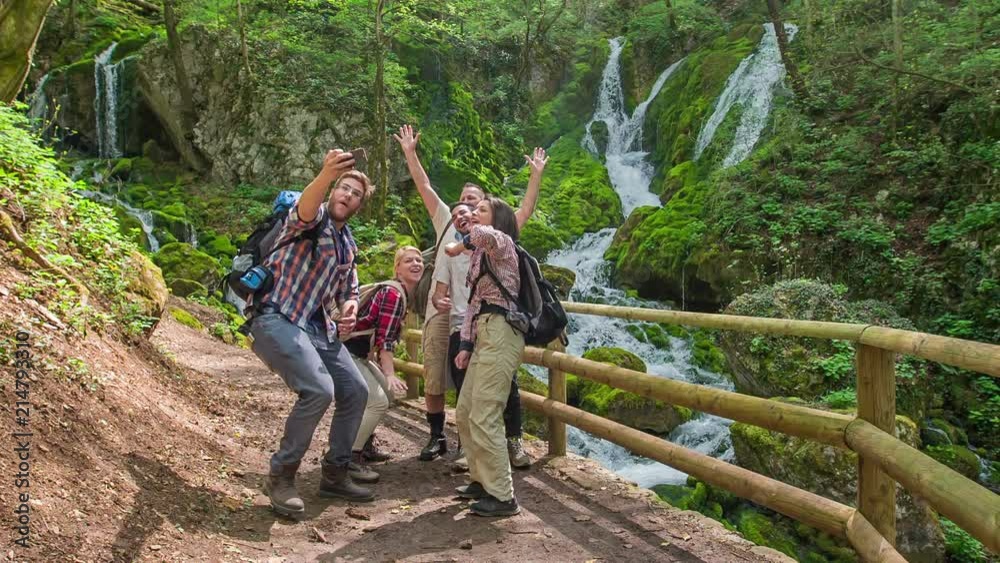 A group of five friends is jumping high up in the air and they're taking a selfie together in front of the waterfall. A group of five friends is jumping high up in the air and they're taking a selfie together in front of the waterfall.