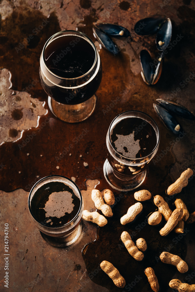 Naklejka premium top view of glasses of cold beer, peanuts and mussels shells on rust surface