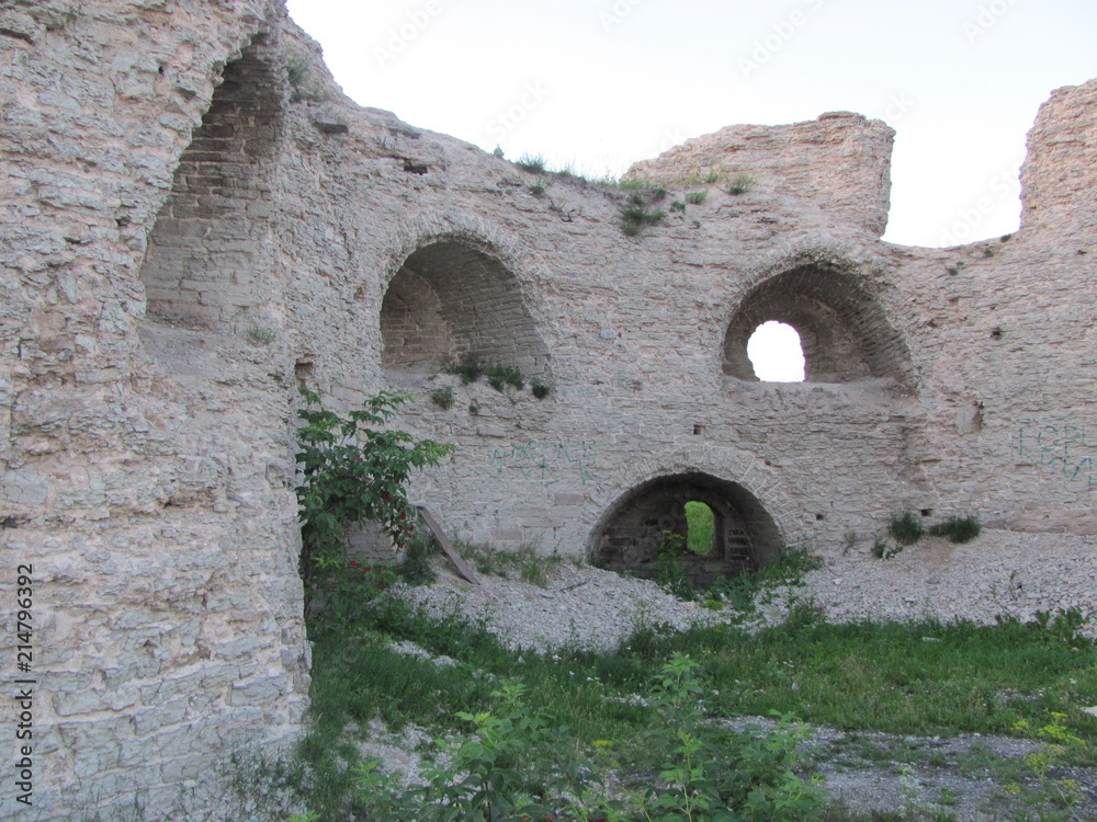 The ruins of a fortress or castle: a white stone wall with openings and niches, covered with green grass