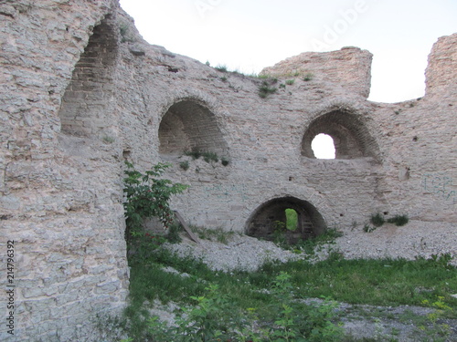 The ruins of a fortress or castle: a white stone wall with openings and niches, covered with green grass © HelenkaNNN