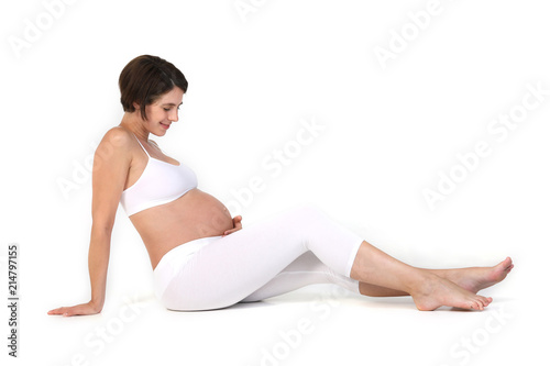 Schwangere Frau sitzt auf dem Boden und hält sich lächelnd den Bauch